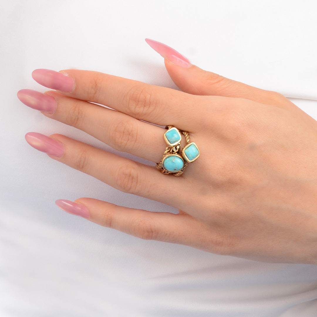 Hand wearing a gold ring with turquoise stones on a white background