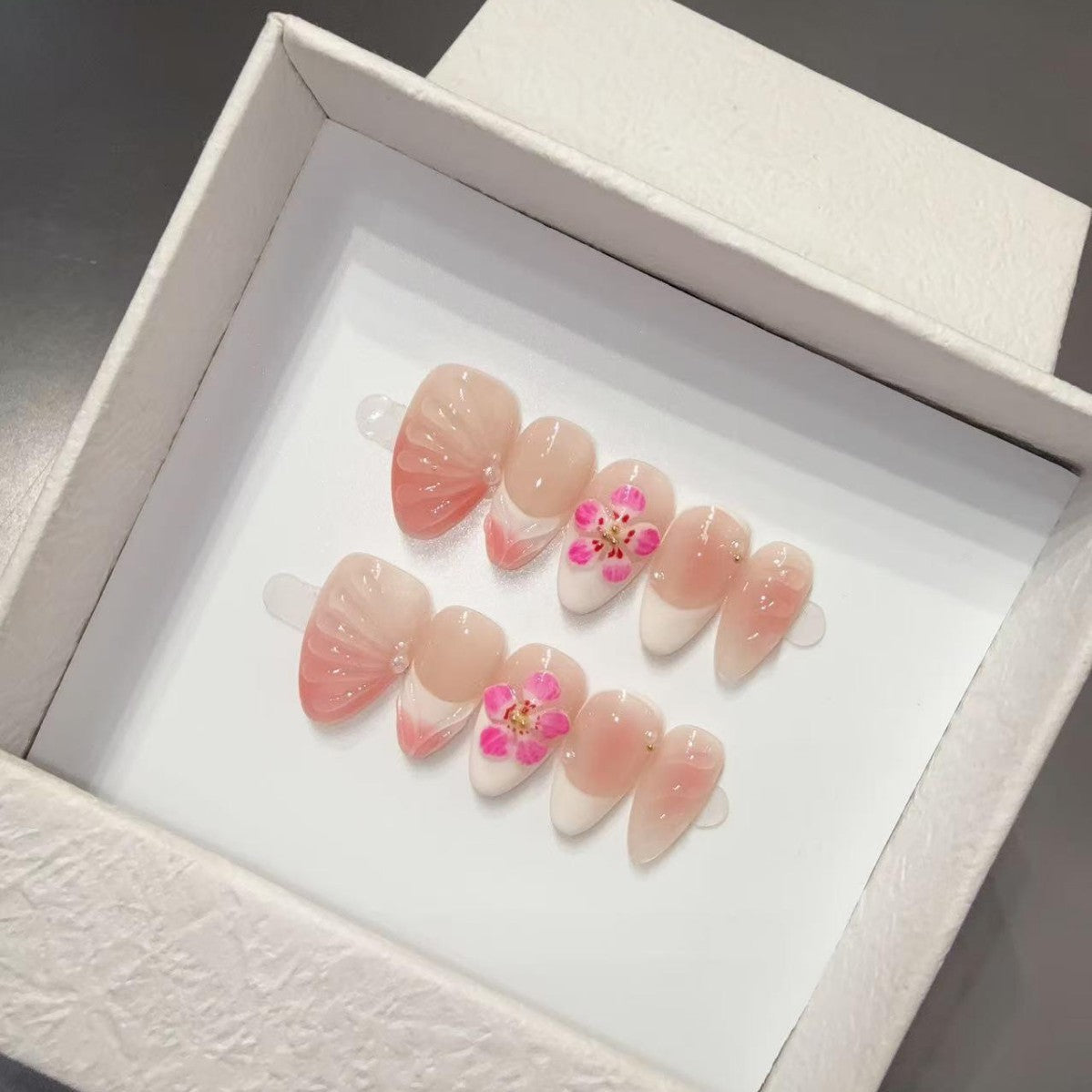Set of pink and white nail floral y2k art designs with floral details in a white box.