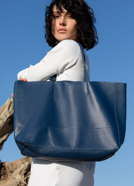 Woman holding a leather vera pelle blue tote bag against a clear blue sky