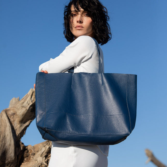 Woman holding a leather vera pelle blue tote bag against a clear blue sky